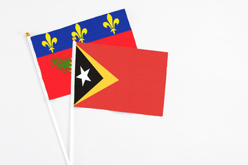 East Timor and Guadeloupe stick flags on white background. High quality fabric, miniature national flag. Peaceful global concept.White floor for copy space.