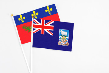 Fototapeta premium Falkland Islands and Guadeloupe stick flags on white background. High quality fabric, miniature national flag. Peaceful global concept.White floor for copy space.