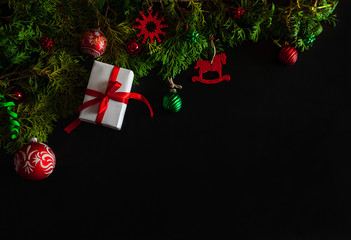 Christmas composition. The border is made of a gift box, branches of thuja, red felt toys, balls and serpentine on a black background. Christmas, winter, New year.