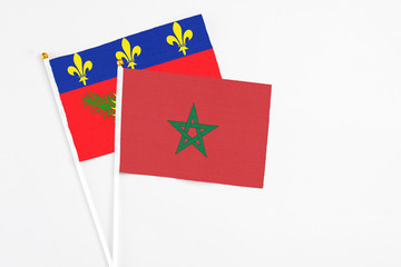 Morocco and Guadeloupe stick flags on white background. High quality fabric, miniature national flag. Peaceful global concept.White floor for copy space.