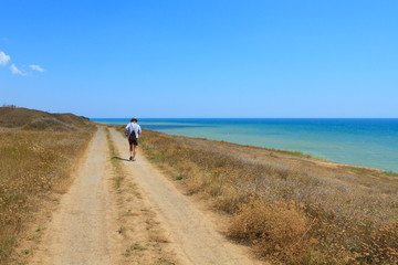 Tourist walks on a dirt road near the sea