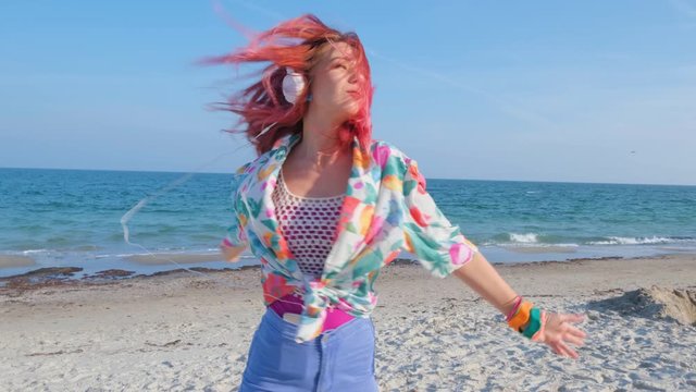 Young woman with colorful hair walk on the summer beach and listen music with headphones 