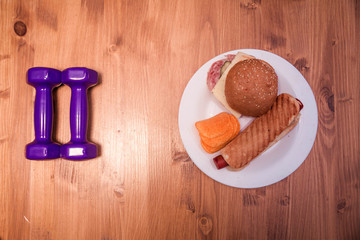 Sports dumbbells and plate with fast food on a wooden background. The choice between sports and fast food