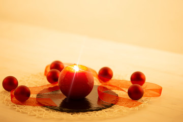 Modern Christmas copy space: close up of a red lit candle with cross screen effect on a limestone plate surrounded by red baubles and a red organza ribbon