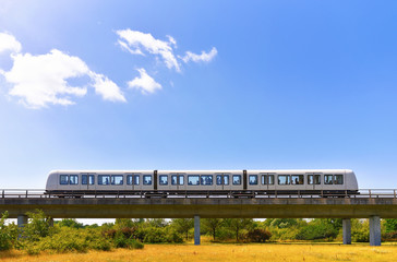 Driverless metro train is moving by overground railroad in countryside area on nature background....