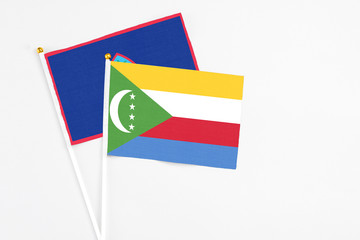 Comoros and Guam stick flags on white background. High quality fabric, miniature national flag. Peaceful global concept.White floor for copy space.