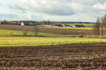 Late autumn. View of the village from the plowed fields. Residential buildings, barns, equipment. Trees in the foreground. Podlasie. Poland.