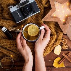 flat lay cozy autumn photo for a blogger with a warm sweater and hands holding tea with lemon, a retro camera and a wooden starry night light.