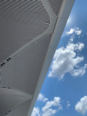 Bottom view of modern architectural ceiling and cloudy blue sky in the background.