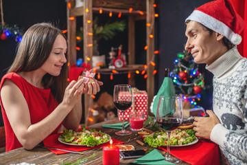 Man is holding a gift box for his beloved. Young couple of lovers spend a festive dinner in the Christmas decorations