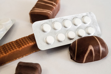 Pill packaging and chocolate candies lie together in pile. Medicaments and sweets.