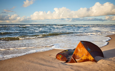 Rusty barrel on a beach at sunset, environment pollution concept.