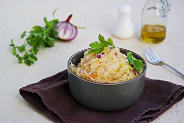 Salad of sauerkraut, carrots and red onions in a brown bowl on a light concrete background. Dressed with sunflower oil. Fermented vegetables recipes. Cabbage salad recipes. Russian cuisine.
