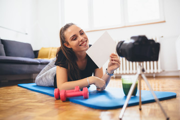 young woman fitness vlogger in her home, holding blank piece of cardboard
