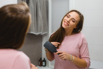 Fototapeta na wymiar young woman brushing or combing hair in bathroom
