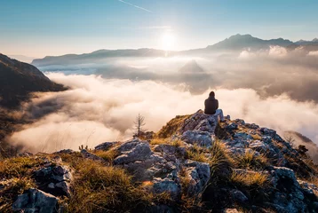 Gordijnen Man sitting an top of mountain at sunrise and enjoying the view © Novak