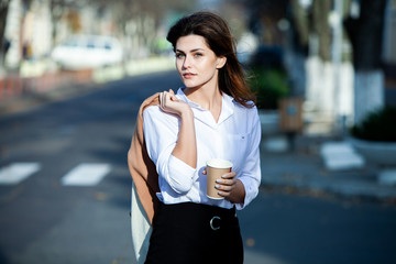 Young stylish woman drinking tea in a city street. Hipster european girl with latte paper glass  in street. Gorgeous young woman with cup of coffee in city street. Coffee break. Coffee to go. 