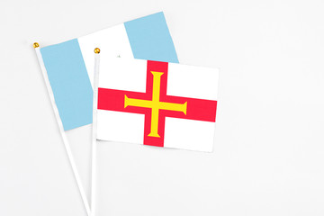 Guernsey and Guatemala stick flags on white background. High quality fabric, miniature national flag. Peaceful global concept.White floor for copy space.