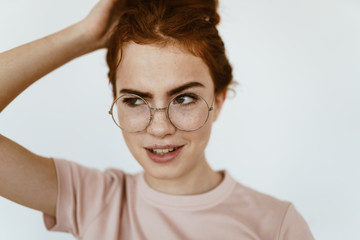 Fototapeta premium schoolgirl looks suspiciously incredulously - mockingly through glasses for sight, raising an eyebrow and holding her hair with her hand on the crown