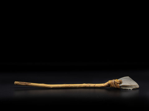 Replicas of the primal stone tool with wooden handles and leather strapping isolated on black background. Primitive stone lance or axe: weapon of the prehistoric peoples.