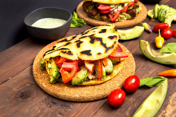 Arepas Vegan - Traditional Colombian Food originally from Latin America arranged on a old rustic wooden table mixed with  vegetable and special avocado sauce
