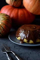 Traditional homemade dessert concept. Pumpkin pudding with chocolate icing and winter squashes on black background