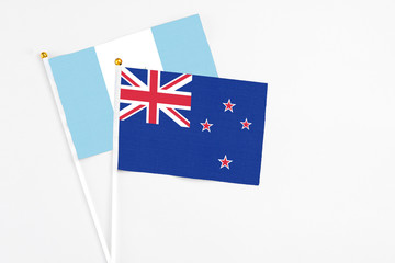 Fototapeta premium New Zealand and Guatemala stick flags on white background. High quality fabric, miniature national flag. Peaceful global concept.White floor for copy space.