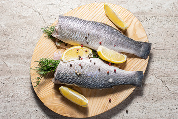 Fresh raw sea bass with dill, lemons and spices on marble kitchen table prepared for cooking. Healthy and organic seafood concept.