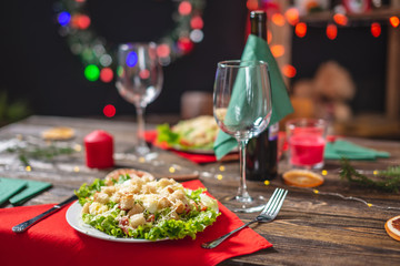 Christmas table with appetizing green Caesar salad with lettuce leaves and a glass on a red napkin on a wooden table