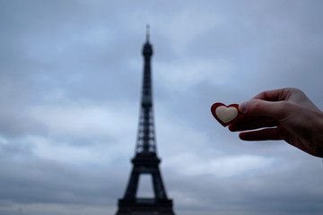 a man's hand holds a heart against the background of the Eiffel tower in Paris, copy space