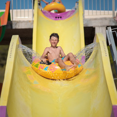Active smiling Caucasian boy in water park in Spain, he sliding down colorful pipe and enjoying his...