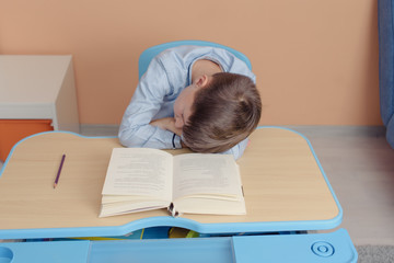 Lazy schoolboy does not want to study. He sleeping on his desk instead of doing home assignment.