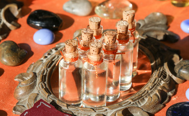 Botellas de cristal con tapones de  corcho para esencias encima de un espejo con fondo de piedras de colores 