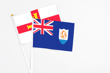 Fototapeta premium Anguilla and Guernsey stick flags on white background. High quality fabric, miniature national flag. Peaceful global concept.White floor for copy space.