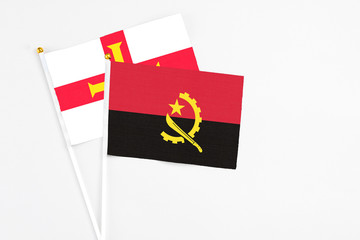 Angola and Guernsey stick flags on white background. High quality fabric, miniature national flag. Peaceful global concept.White floor for copy space.