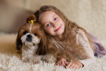 Happy smiling little girl hugging a dog Shih Tzu at home