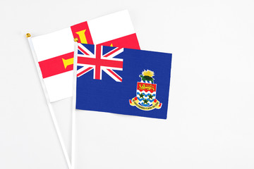 Fototapeta premium Cayman Islands and Guernsey stick flags on white background. High quality fabric, miniature national flag. Peaceful global concept.White floor for copy space.