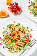 Fresh green organic salad with raw ingredients close up. Tasty salad with arugula, orange slices, pomegranate and cheese on white plate, top view. Healthy eating, dieting concept