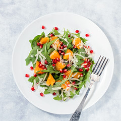 Fresh green organic salad with raw ingredients close up. Tasty salad with arugula, orange slices, pomegranate and cheese on white plate, top view. Healthy eating, dieting concept