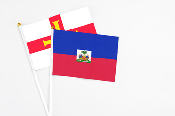 Haiti and Guernsey stick flags on white background. High quality fabric, miniature national flag. Peaceful global concept.White floor for copy space.