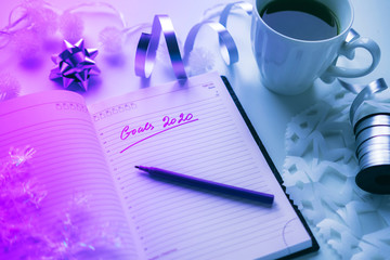 2020 goals written on a diary with light, hot coffe or tea and decoration. Happy New Year and motivation consept. Neon background