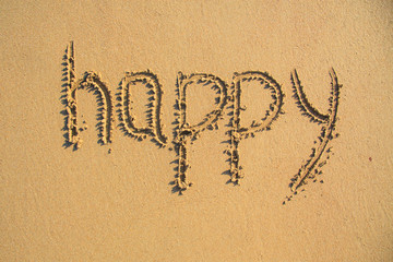 Word HAPPY drawn on the sand of sandy beach.