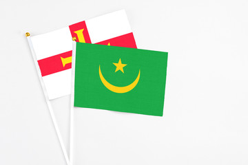 Mauritania and Guernsey stick flags on white background. High quality fabric, miniature national flag. Peaceful global concept.White floor for copy space.