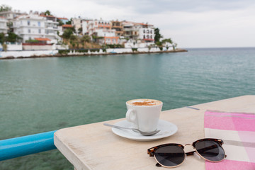 Cup of cappuccino in a cafe terrace on wooden table with blurred landscape on the background.