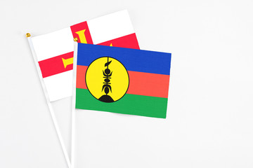 Obraz premium New Caledonia and Guernsey stick flags on white background. High quality fabric, miniature national flag. Peaceful global concept.White floor for copy space.