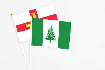Norfolk Island and Guernsey stick flags on white background. High quality fabric, miniature national flag. Peaceful global concept.White floor for copy space.