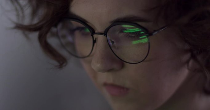 Hacker Woman Tries to Get Confidential Information. Pretty hacker woman attacks confidational data using programme code. We see the reflection of the code in her glasses
