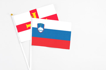 Slovenia and Guernsey stick flags on white background. High quality fabric, miniature national flag. Peaceful global concept.White floor for copy space.
