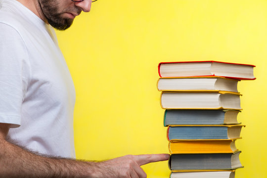 Concept of education. A man in a white t-shirt points to the penultimate book in the pile. Yellow background