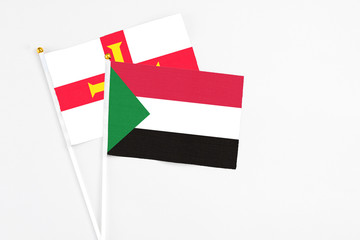 Sudan and Guernsey stick flags on white background. High quality fabric, miniature national flag. Peaceful global concept.White floor for copy space.